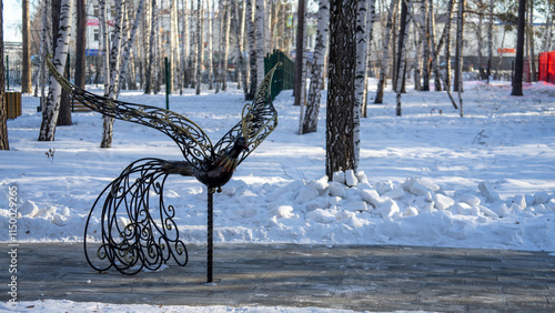 Bronze sculpture of fabulous bird in city park Manin Park in city of Verkhnyaya Pyshma on winter day against backdrop of birch trees and snowdrifts photo