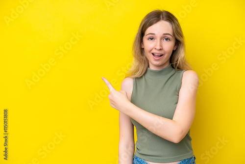 Blonde English young girl isolated on yellow background surprised and pointing side