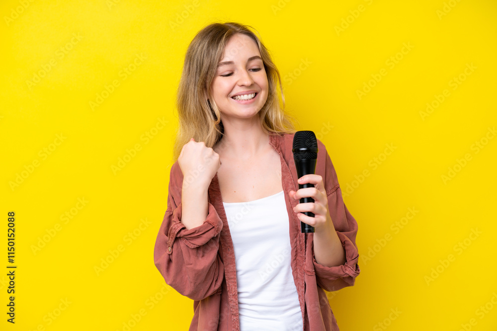 Young singer caucasian woman picking up a microphone isolated on yellow background celebrating a victory Young singer caucasian woman picking up a microphone isolated on yellow background celebrating a victory