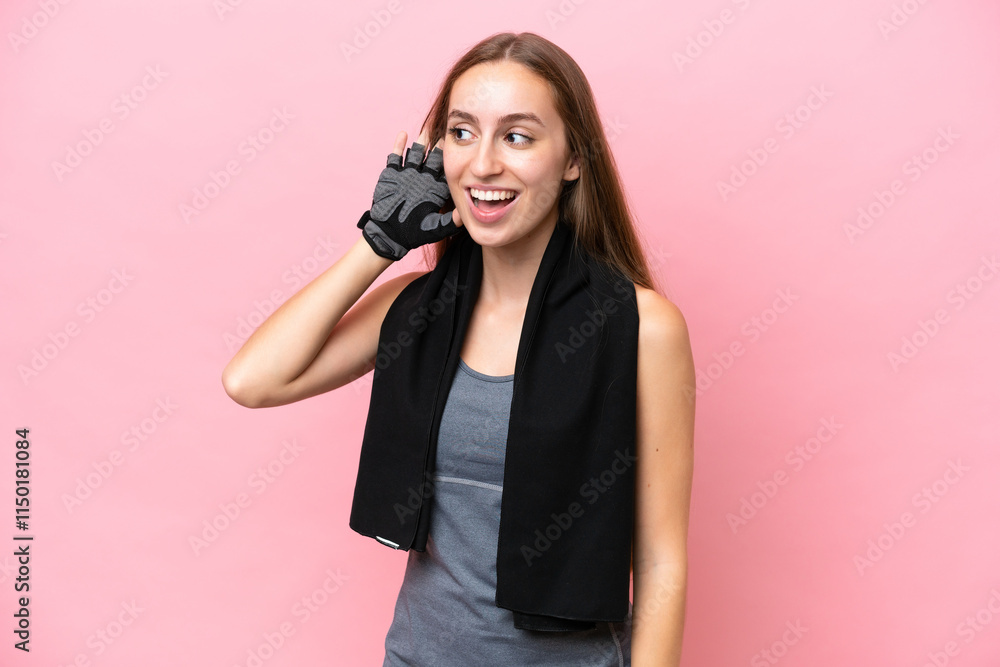 Fototapeta premium Young sport caucasian woman wearing a towel isolated on pink background listening to something by putting hand on the ear