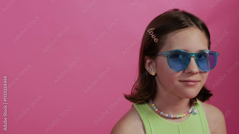 Close-up portrait of gen alpha girl adjusting blue glasses and smiling for camera while standing against pink background Close-up portrait of gen alpha girl adjusting blue glasses and smiling for camera while standing against pink background