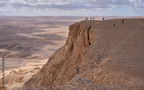Majestic mountain landscape in Nahal Ashosh Nature Reserve, Negev Desert. Orange sandstone hills and mountain folds. Hikers standing in a cliff. The trails less travelled. Outdoor activity.