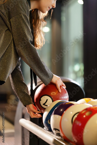 Close-up of the hands of a young woman choosing a suitable ball for her turn in the bowling competition at the bowling alley.