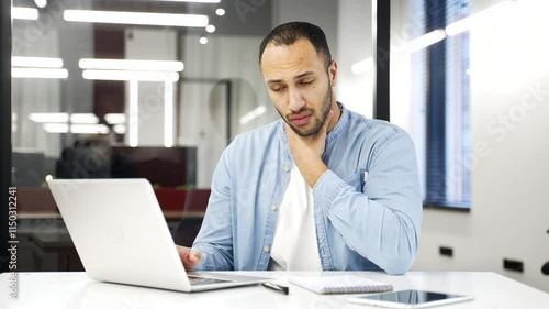 Wallpaper Mural Sick young adult African American businessman suffering from a sore throat while working on a laptop sitting at a workplace in a business office. Worker has a cold, virus or flu, massaging a sore spot Torontodigital.ca