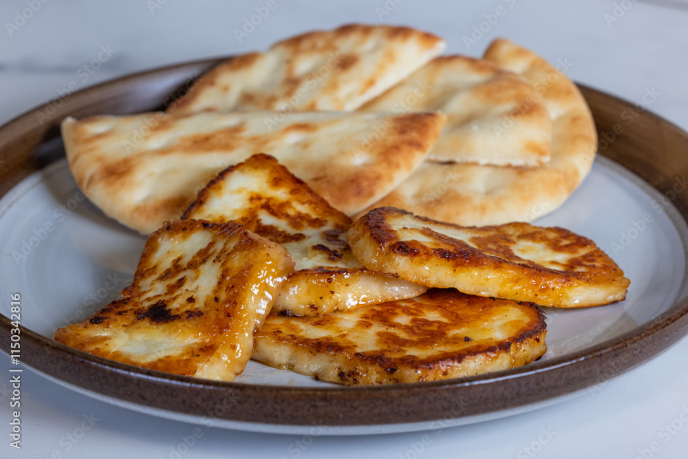 A plate of fried halloumi cheese with a side of pita bread. The food is golden brown and looks delicious. A plate of fried halloumi cheese with a side of pita bread. The food is golden brown and looks delicious.