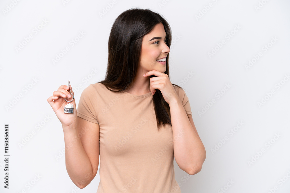 Young Brazilian woman holding home keys isolated on white background thinking an idea and looking side Young Brazilian woman holding home keys isolated on white background thinking an idea and looking side