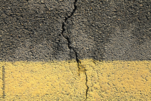 Asphalt surface and backdrop. Asphalt with a crack in middle. Road background with a yellow dividing stripe at the bottom. Detailed texture of bitumen close-up. Wet road foundation that needs repair photo