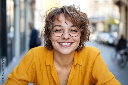 Joyful woman smiling in yellow shirt at outdoor cafe during a sunny day in a vibrant city street