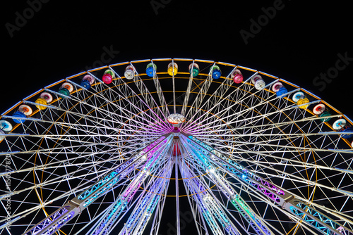 Low angle view from below of a Ferris wheel illuminated with colorful lights with the sky completely dark at night photo