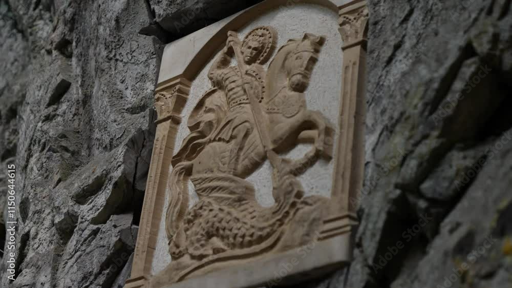Saint George stone icon displayed on a natural rock wall. Curved stone old icon of Saint George is set on a natural rock wall, showcasing spirituality and artistry, handheld shot. Saint George stone icon displayed on a natural rock wall. Curved stone old icon of Saint George is set on a natural rock wall, showcasing spirituality and artistry, handheld shot.