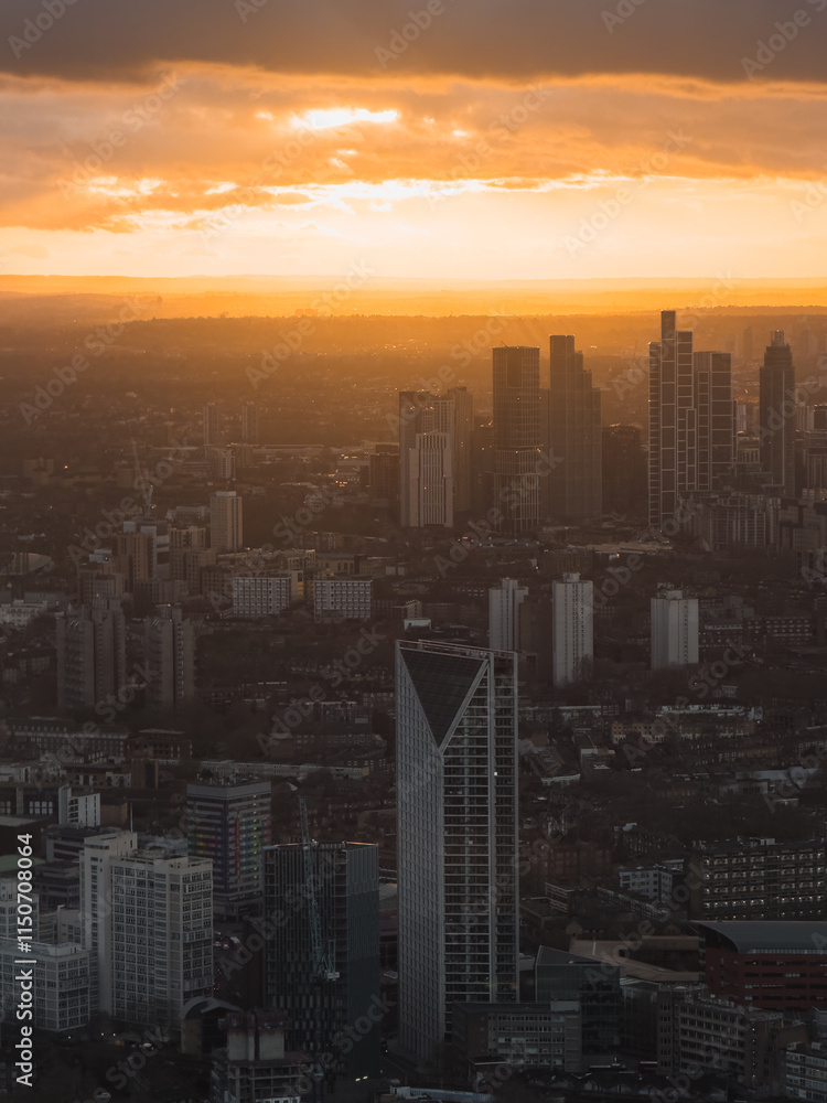 Fototapeta premium The image shows London's skyline during sunset, featuring silhouetted skyscrapers against a vibrant orange and gold sky, highlighting urban architecture.
