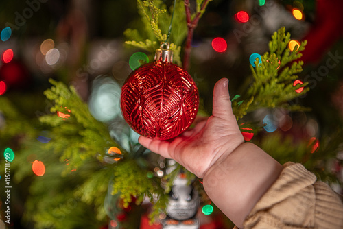 baby hand grabbing red Christmas bulb on decorated tree 