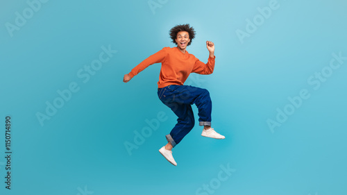 Картината върху платно A young African American man with curly hair is jumping joyfully against a vibrant blue background