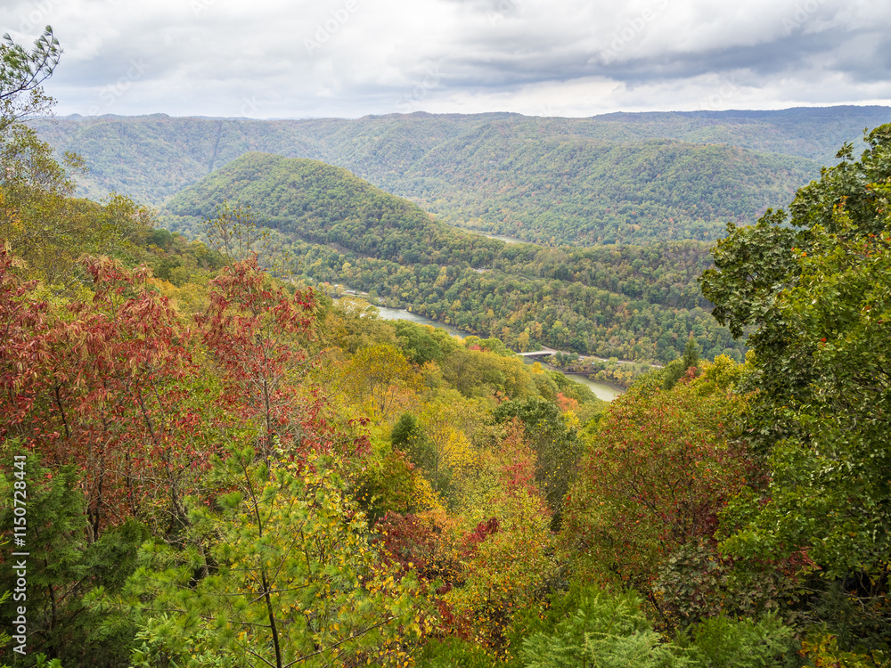 The mountains at New River Gorge National Park, covered in early fall colors, stretch towards the horizon with bridges in the distance and clouds drifting overhead. The mountains at New River Gorge National Park, covered in early fall colors, stretch towards the horizon with bridges in the distance and clouds drifting overhead.