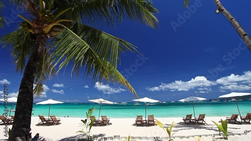 Sun umbrellas and beach chairs on tropical beach with palm trees. Summer vacation. Boracay