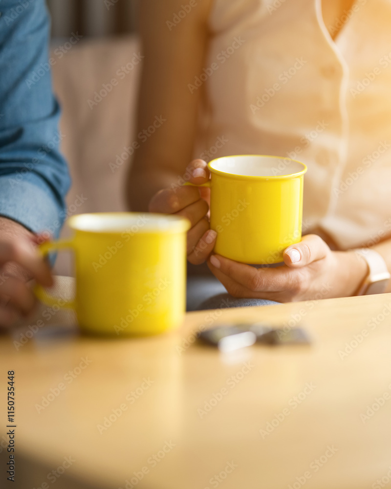 Yellow mugs with tea, coffee, chicory in hands at table. Man and woman drinking tea. Ceramic glossy cups. Coffee break. Meet for tea in cafe. Morning rituals. Food and Drink Concept. Warm atmosphere. Yellow mugs with tea, coffee, chicory in hands at table. Man and woman drinking tea. Ceramic glossy cups. Coffee break. Meet for tea in cafe. Morning rituals. Food and Drink Concept. Warm atmosphere.