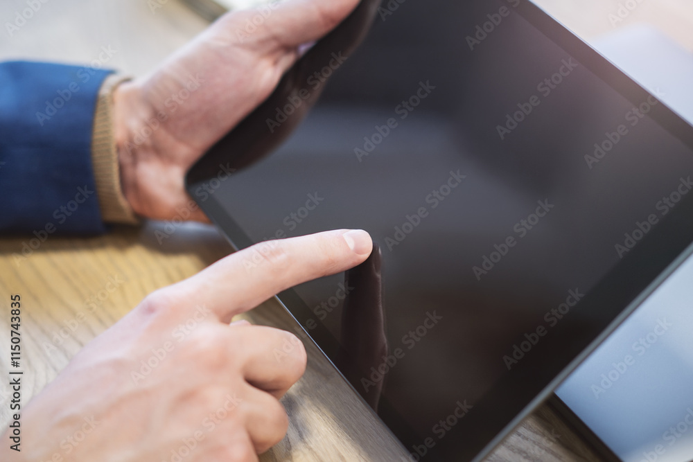 Detailed image of a male hand interacting with a digital tablet on a desk, amidst the vague surroundings of a bright office setting Detailed image of a male hand interacting with a digital tablet on a desk, amidst the vague surroundings of a bright office setting