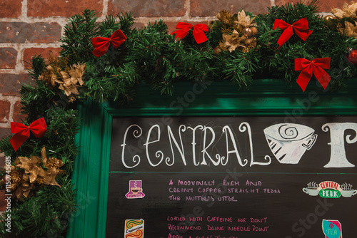 Vászonkép A chalkboard sign displays the Central Perk logo with green garlands, red bows, and gold accents against a brick wall, part of a themed setup in London