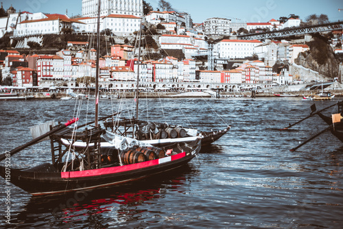 Traditional Portuguese Rabelo boat loaded with wooden wine barrels, docked on the Douro River in Porto, Portugal, with colorful Ribeira waterfront buildings in the background photo