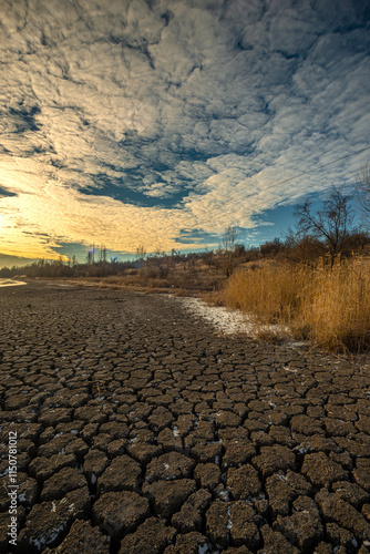 Dry pond at the winter morning,lansdcape with pond and froxen dirt. Beautiful clouds in the sky , reed on the beach .Sunlights through the trees, snow on the ground with ice, enviroment on the lake.