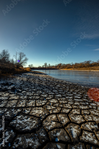 Feozen pond at the winter day,lake with ice,dry ground near the lake.Sun in the sky, sunlights and sky with blue clouds.Blue winter colors , wild nature with a pond.Frozen beach near the lake,snowy  photo