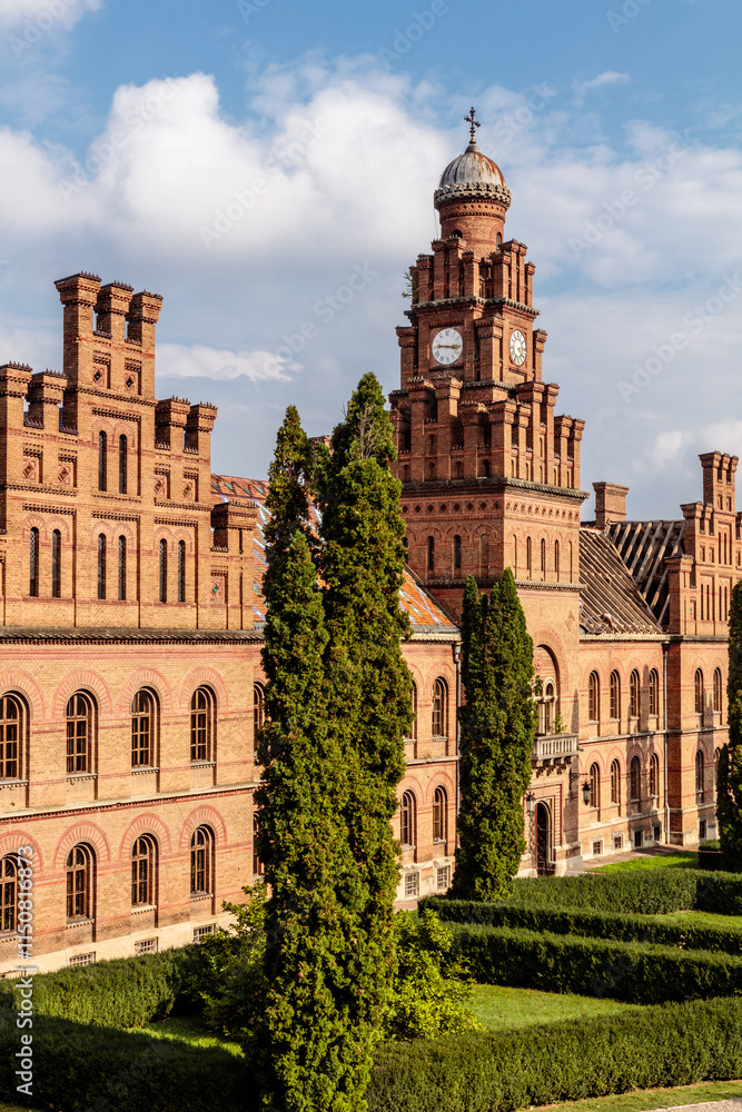 A large brick building with a clock tower and a large tree in front of it A large brick building with a clock tower and a large tree in front of it