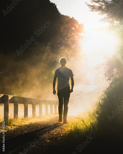 A man walking along a misty road catching the golden morning light