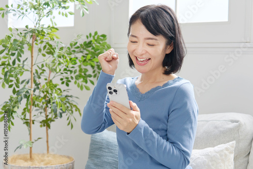 スマホを持つ中年女性　ガッツポーズ　リビング photo