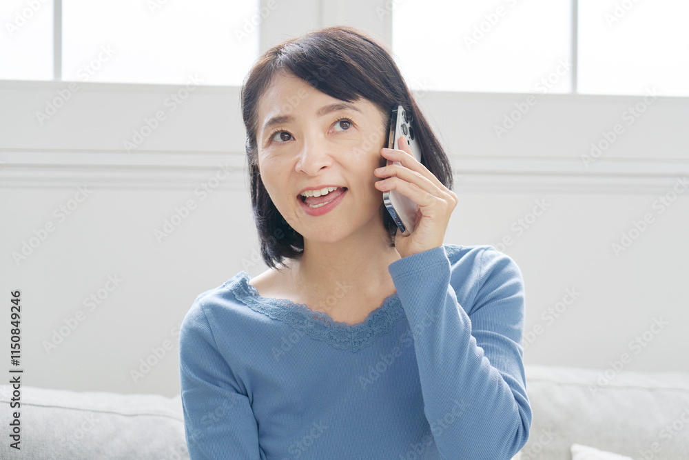 スマホで電話する中年女性 リビング スマホで電話する中年女性 リビング