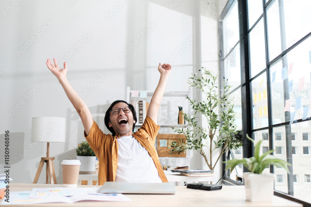 Male Asian freelance worker raises his fists and relieved after finishing deadline works in casual small business office, satisfied online startup jobs with laptop, E-commerce SME career satisfaction. Male Asian freelance worker raises his fists and relieved after finishing deadline works in casual small business office, satisfied online startup jobs with laptop, E-commerce SME career satisfaction.