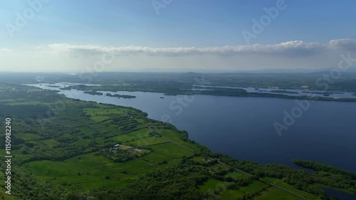 Lower Lough Erne, County Fermanagh, Northern Ireland, June 2023. Drone slowly pulls backwards in a wide aerial view above the lush green forest with the picturesque lake in the distance on a clear day photo