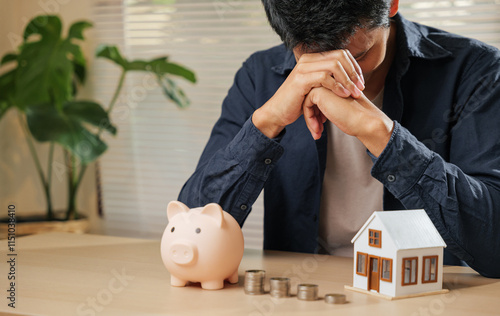 Stressed man holding his forehead, surrounded by a piggy bank, coin stacks, and a house model. Captures the struggles of money issues, financial risks, property concerns