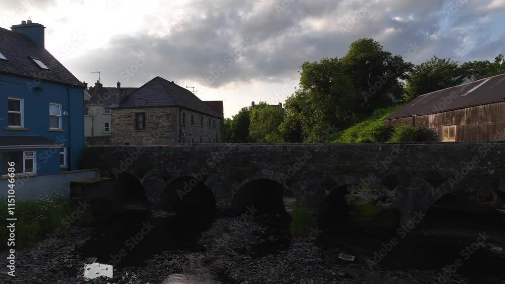 Pettigo, County Donegal, Northern Ireland, June 2023. Drone ascends above the river Termon with a stone bridge on the Irish Border with Northern Ireland as sun flare glistens above the slate roof tops Pettigo, County Donegal, Northern Ireland, June 2023. Drone ascends above the river Termon with a stone bridge on the Irish Border with Northern Ireland as sun flare glistens above the slate roof tops