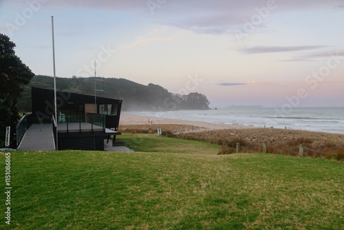 Coastal beach scene at sunset. People relax on the shore near a surf lifesaving club. Tranquil atmosphere. ONEMANA, COROMANDEL PENINSULA, NEW ZEALAND photo