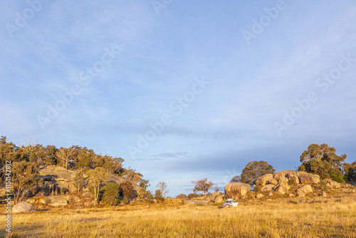 Canvas-taulu Landscape of granite rock formations with trees in the late afternoon sun, with a four wheel drive for size comparison and under a blue sky with clouds near Tenterfield in New South Wales, Australia