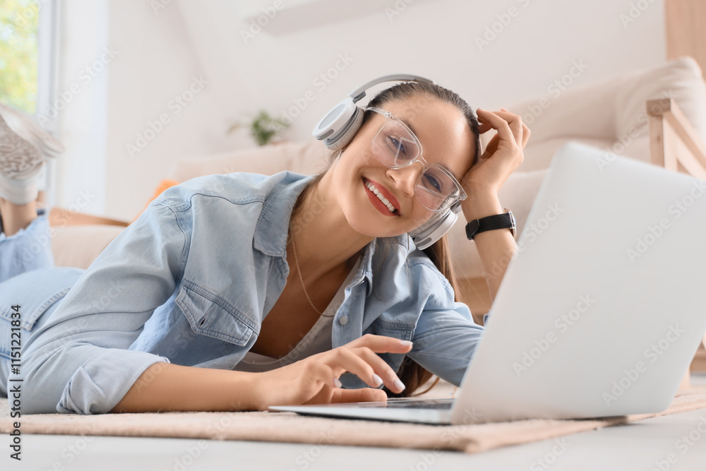 Young woman in headphones using laptop on carpet at home Young woman in headphones using laptop on carpet at home
