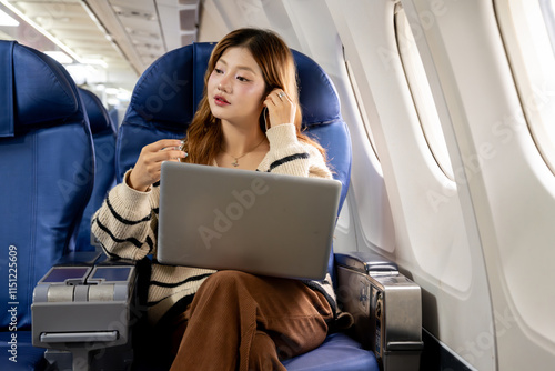 Asian woman sitting watching a movie on her laptop on an airplane while traveling somewhere during her vacation.
