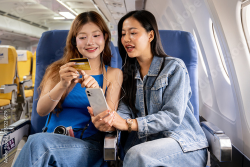 Two cheerful Asian women discuss the convenience of their credit card lifestyle during a flight.