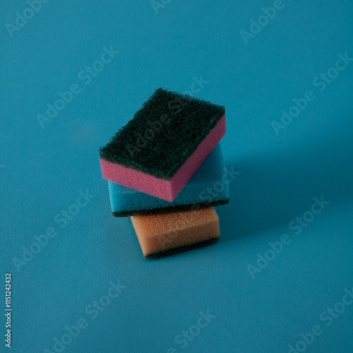 In the blue water three small pink, blue and orange colored sponges are submerged waiting to clean the dirty and dusty surfaces photo