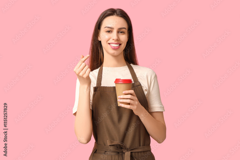 Young female barista with cup of coffee making heart gesture on pink background Young female barista with cup of coffee making heart gesture on pink background