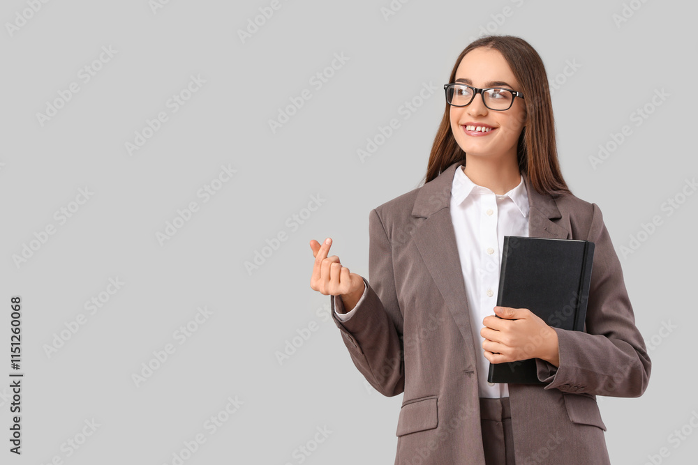 Beautiful young woman holding book and making heart with her fingers on grey background Beautiful young woman holding book and making heart with her fingers on grey background