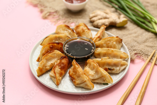 Plate with fried Japanese gyoza and bowl of soy sauce on pink background, closeup