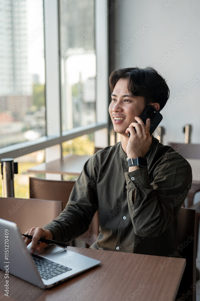 Obraz premium A positive Asian businessman talking on the phone while working remotely from a coffee shop.