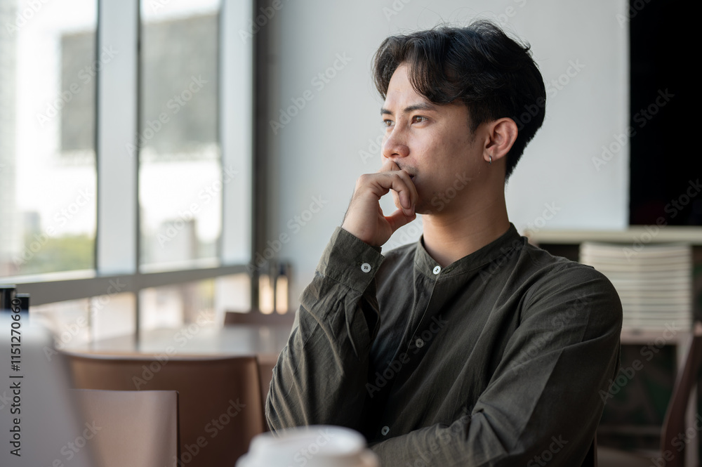 A thoughtful Asian businessman admiring the view outside with a serious expression while working. A thoughtful Asian businessman admiring the view outside with a serious expression while working.