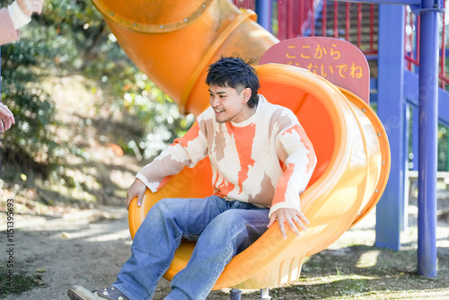 In a large park in Handa City, Aichi Prefecture, a couple in their 20s are having fun on the slide while taking selfies with a small camera. photo