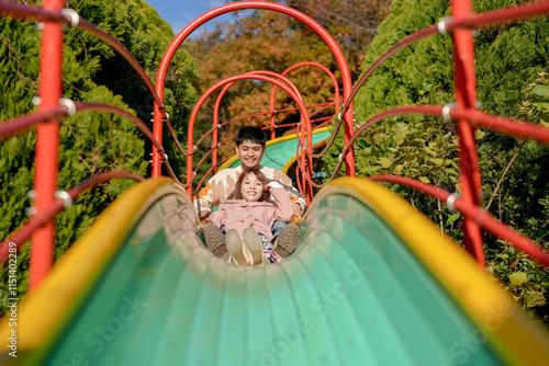 In a large park in Handa City, Aichi Prefecture, a couple in their 20s are having fun on the slide while taking selfies with a small camera. photo