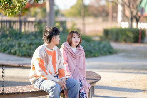 A couple in their 20s are sitting on a bench and talking in a large park in Handa City, Aichi Prefecture in autumn. photo