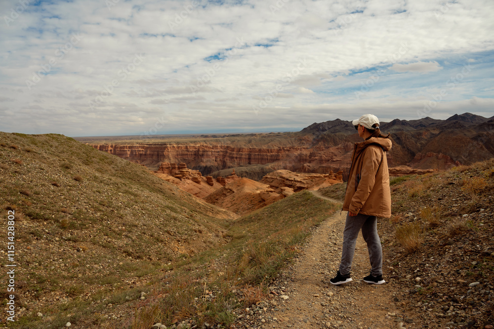 Naklejka premium female tourist on the trail looking at the beautiful orange canyon mountains and cloudy sky