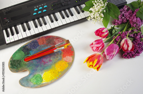 Synthesizer keyboard, art palette, brushes, a bouquet of tulips on a light background.