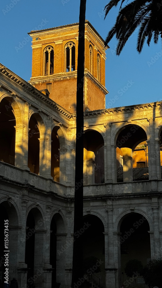 Obraz premium The stunning historic architecture, bathed in the warm hues of sunset, stands proudly in an ancient courtyard embraced by lush palm trees